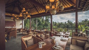 An outdoor restaurant with wooden furniture, hanging light fixtures, and a view of lush greenery. - Asvara Resort & Spa Ubud by Ini Vie Hospitality (Ubud)