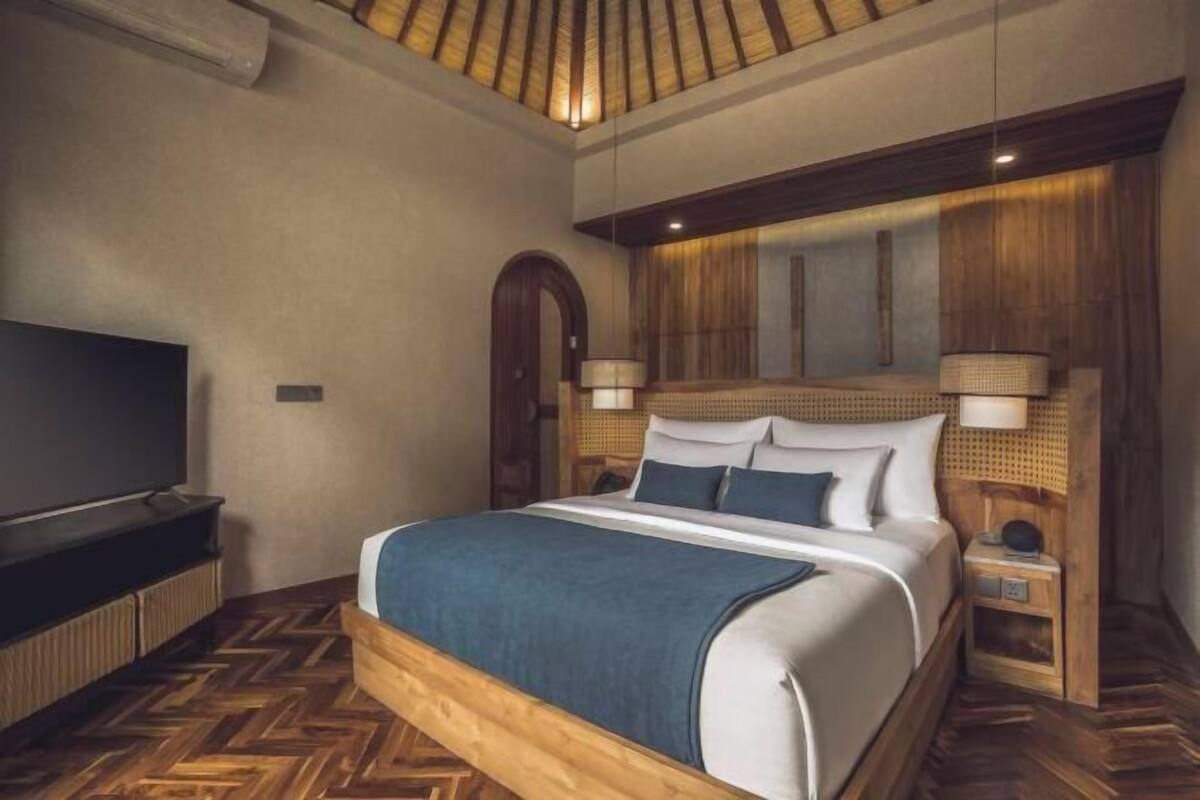 A bedroom with a large bed, wooden headboard, two bedside lamps, a TV, and a herringbone-patterned floor.