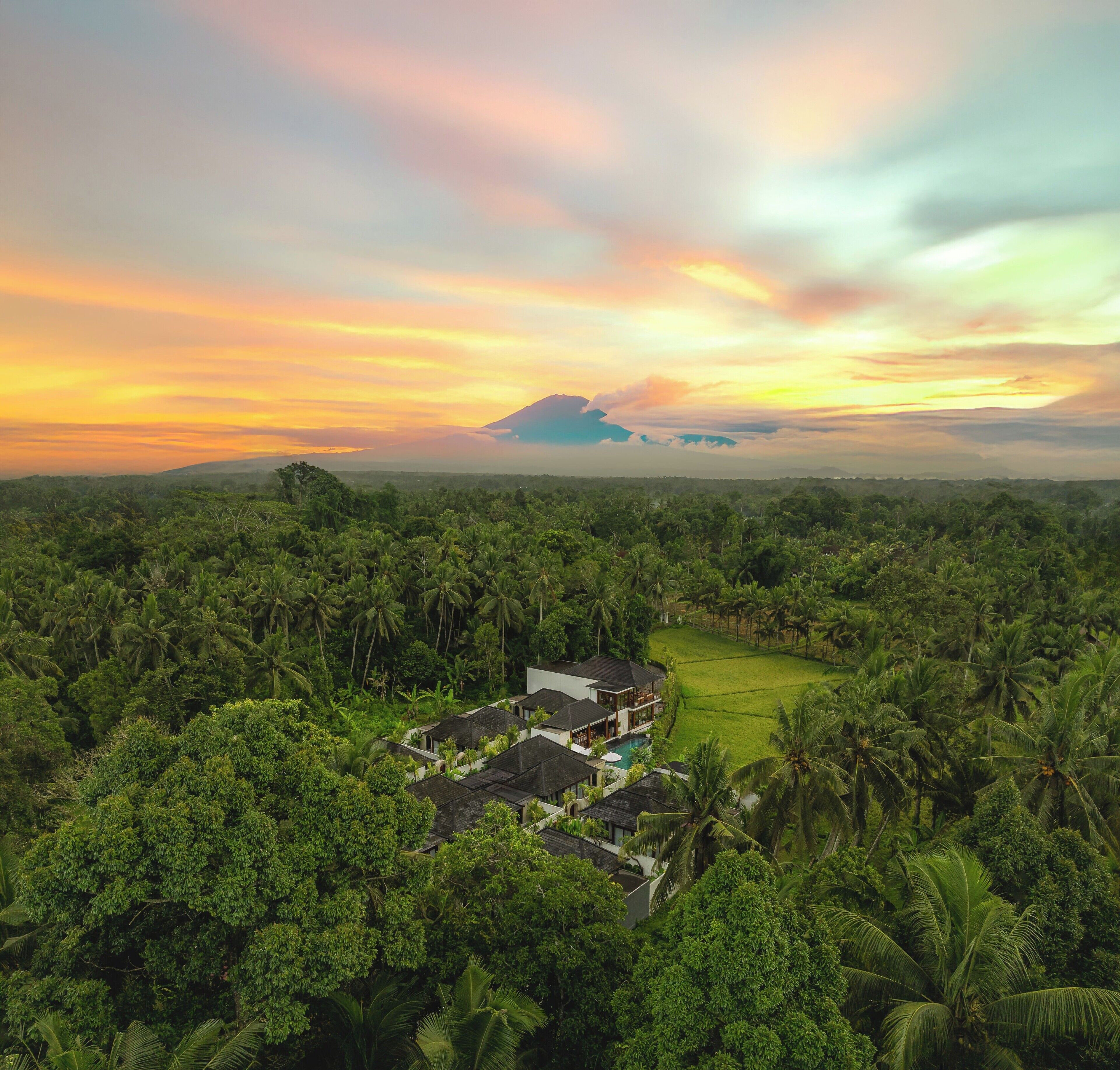 Trooppinen lomakeskus, jossa on uima-allas, ja jota ympäröivät tiheät palmulehdot ja taustalla kohoava vuori.