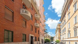 A narrow street lined with multi-story buildings, featuring balconies and a clear blue sky.