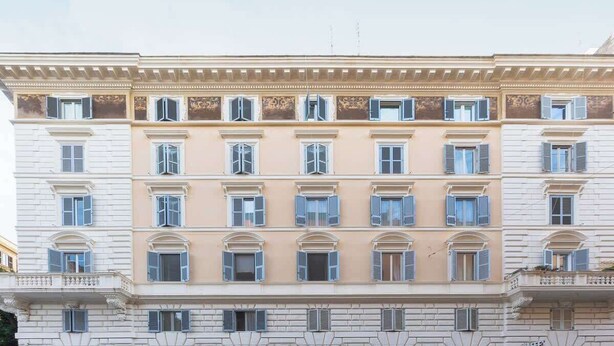 Un edificio de varios pisos con una fachada simétrica, ventanas distribuidas uniformemente y un balcón central.