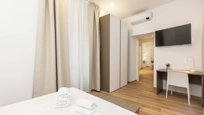 Una habitación de hotel moderna con cama, escritorio, televisor y zona de ducha.