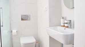 Un baño moderno con inodoro blanco, lavamanos con espejo y zona de ducha.