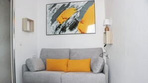 Un sofá gris con dos cojines amarillo mostaza, un cuadro abstracto moderno encima y una lámpara de pared a la derecha.