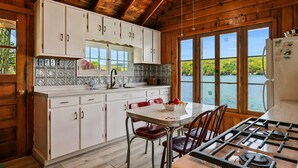 Uma cozinha com armários de madeira, uma mesa de jantar com cadeiras, um fogão e vista para um lago.