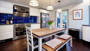 Une cuisine moderne dotée d’appareils électroménagers en acier inoxydable, d’une table en bois et de luminaires suspendus.