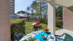 Un patio con mesa lista para comer, rodeado de follaje y vistas a un edificio y árboles.