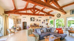 A spacious living room with exposed wooden beams, a large grey sofa, a green armchair, and a dining area with a table and chairs. - Villa Alizée in St Tropez, Private swimming pool, Near town center (Gassin)