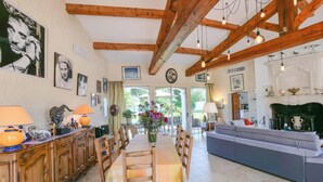 A spacious living room with a dining area, wooden beams, a fireplace, and a view of the outdoors. - Villa Alizée in St Tropez, Private swimming pool, Near town center (Gassin)