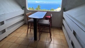 A small, enclosed room with a table and chairs, a window with a view of the sea, and a tiled floor. - 15 minutes from the beaches of St Leu or Étang Salé. Sea view apartment with swimming pool. (Saint-Leu)