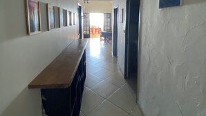 A hallway with a long counter, tiled floor, and a high ceiling. There are framed pictures on the walls and a painting on the right wall. - 15 minutes from the beaches of St Leu or Étang Salé. Sea view apartment with swimming pool. (Saint-Leu)