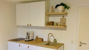 A compact kitchen with white cabinets, a wooden countertop, a sink, and a small shelf with decorative items.