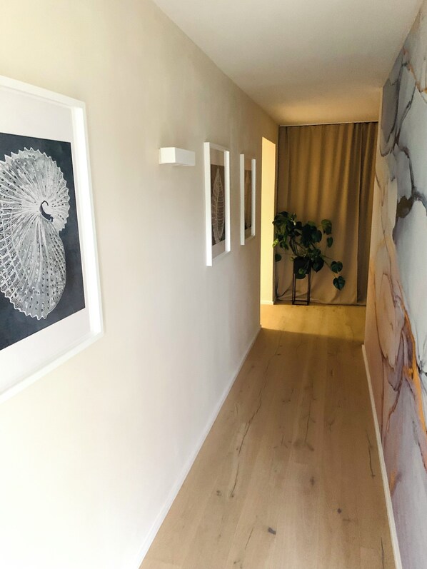 Un pasillo con obras de arte enmarcadas, una planta y una pared de mármol.