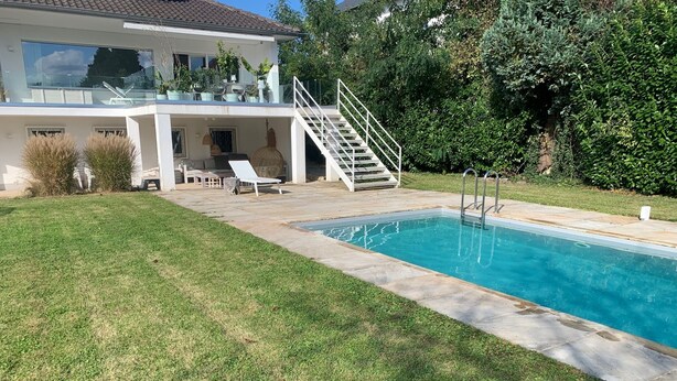 A modern house with a swimming pool, a covered patio, and a staircase leading to a balcony.