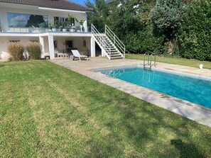 Una casa moderna con piscina, un porche cubierto y una escalera que lleva a un balcón.