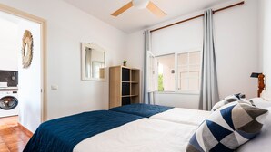 A bedroom with a bed, a ceiling fan, a window with curtains, a wardrobe, and a washing machine in the adjacent room. - CASTELLSOL 201 (Arenal d´en Castell)