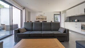 A modern living room with a grey sofa, a wooden coffee table, and a large window with curtains.