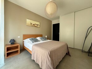 A bedroom with a bed, bedside table, lamp, artwork, and a wardrobe.
