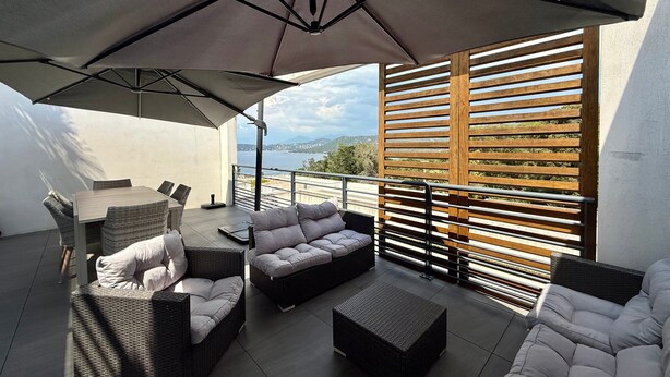 A balcony with wicker furniture, a table, and a view of the sea.