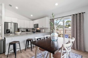 A modern kitchen with white cabinets, stainless steel appliances, and a dining area with a dark wooden table and white chairs.