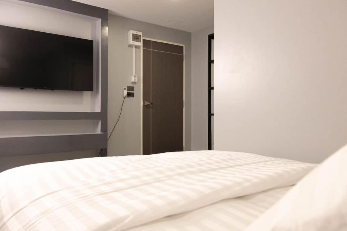 A hotel room with a bed, a mounted TV, and a door.