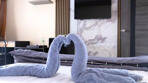 A neatly made bed with a swan-shaped towel arrangement in a modern hotel room with a flat-screen TV mounted on the wall. - Cabanaz Pool Villa (Bangkok)