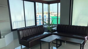 A modern living room with a sofa, a coffee table, and large windows offering a view of buildings and a construction site. - Cabanaz Pool Villa (Bangkok)