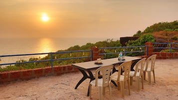 A table with chairs set up on a sandy surface, overlooking a body of water during sunset.
