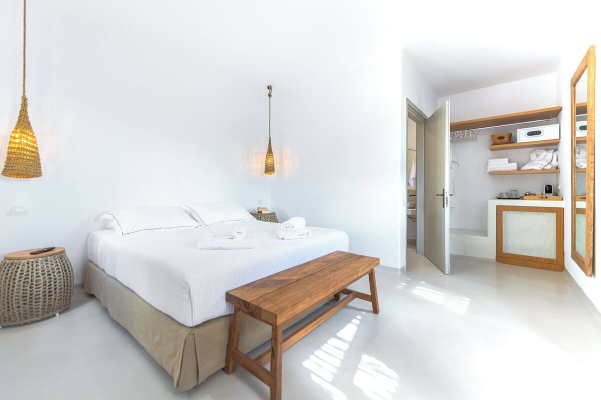 A modern bedroom with a bed, bedside table, hanging light, and a walk-in closet.