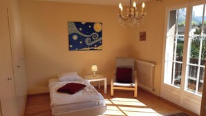 Une chambre à coucher comprenant un lit, une chaise, une table, un lustre et une grande fenêtre donnant sur un paysage montagneux.