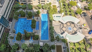 Vue aérienne d’un bâtiment moderne doté d’une piscine centrale, de jardins aménagés et d’une place circulaire.
