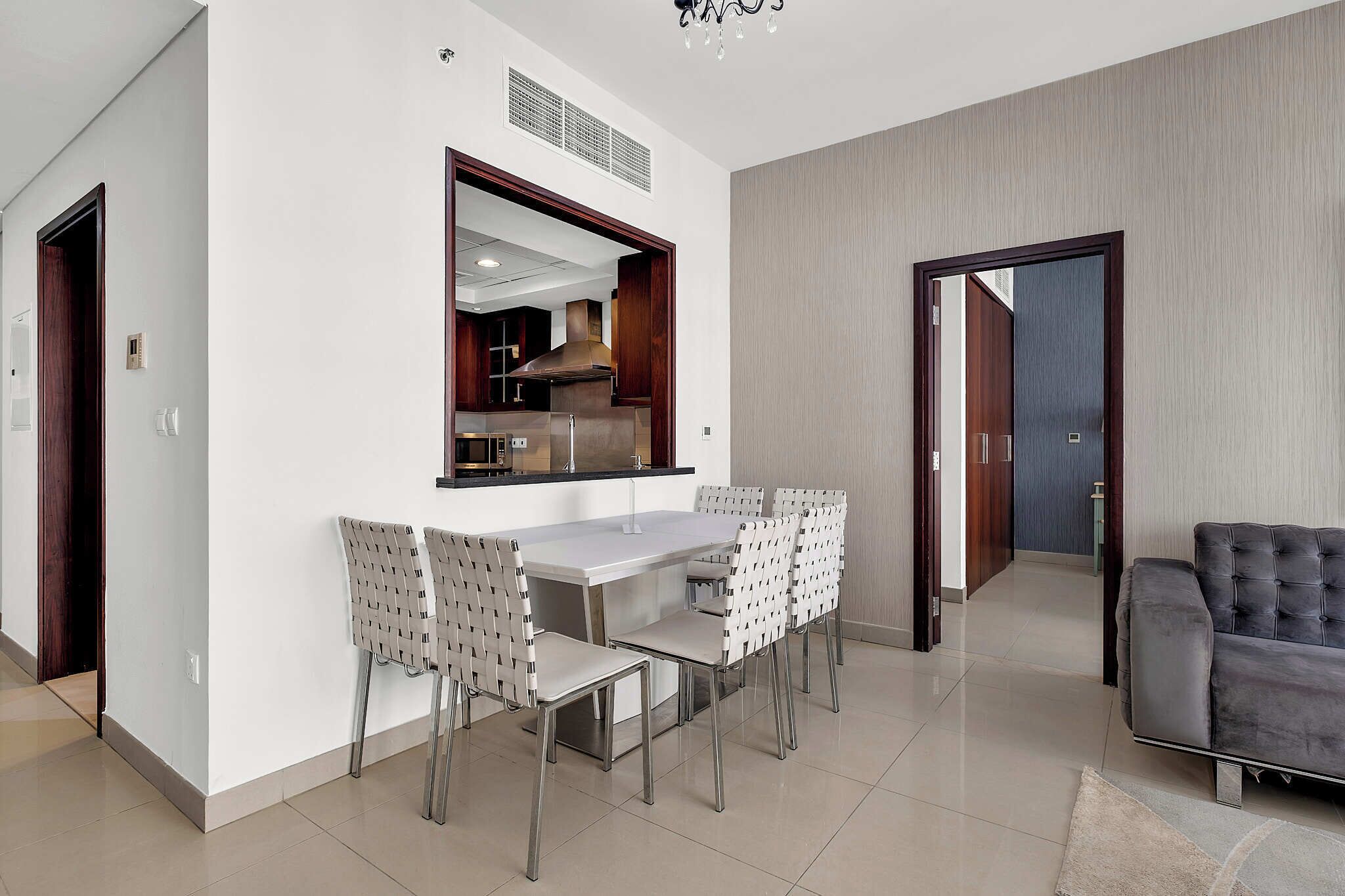 A modern living room with a dining area, a sofa, and a kitchen visible through an open door.