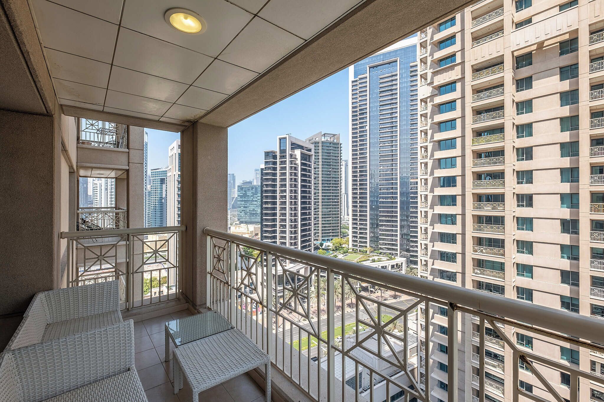 Un balcone con mobili in vimini bianco, ringhiera in metallo e vista su edifici alti.
