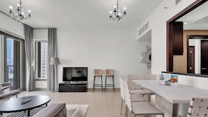 Un salon moderne comprenant un canapé, une table basse ronde, un téléviseur, deux tabourets de bar, une table à manger avec des chaises et un lustre.