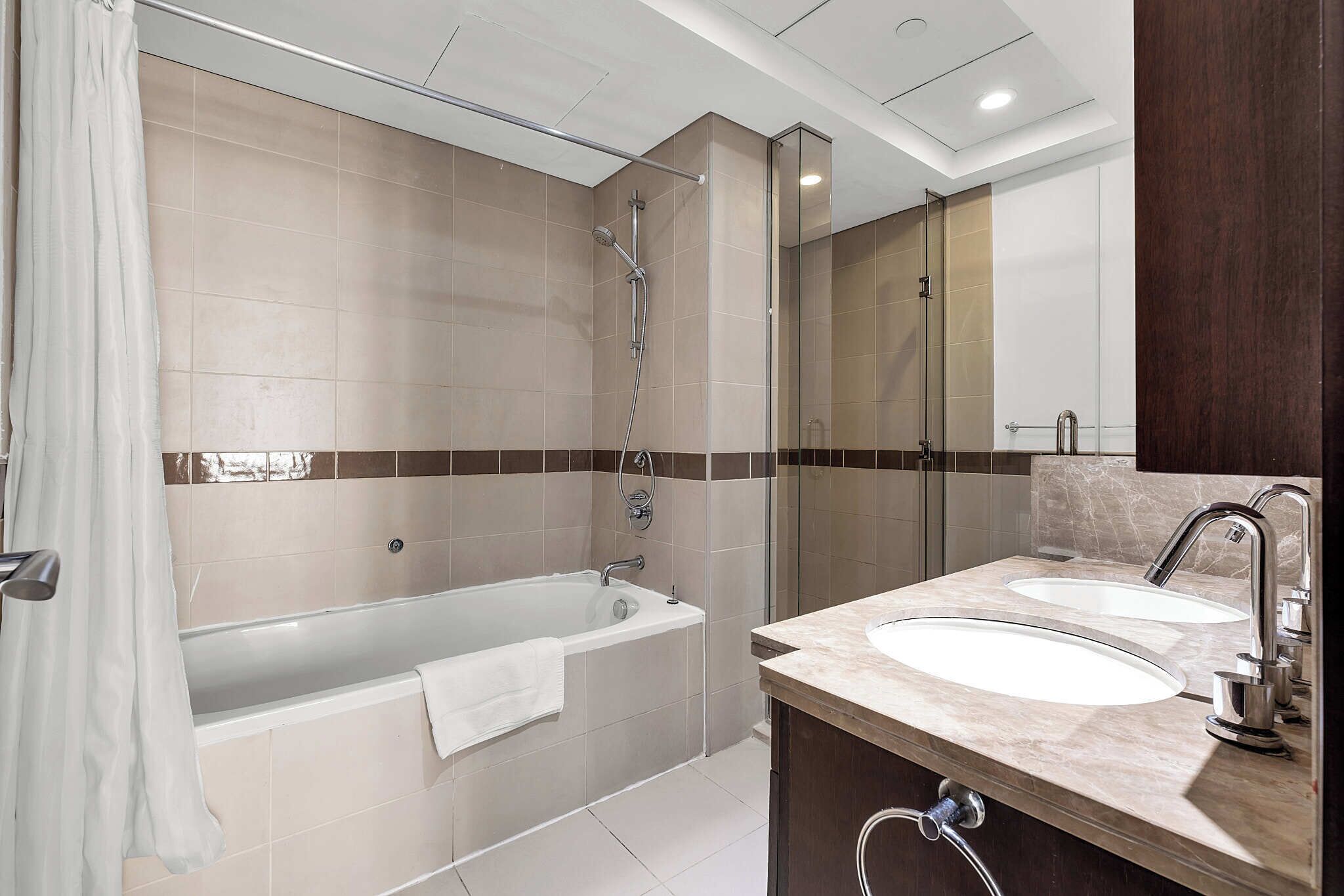 A modern bathroom with a bathtub, two sinks, and a glass shower enclosure.