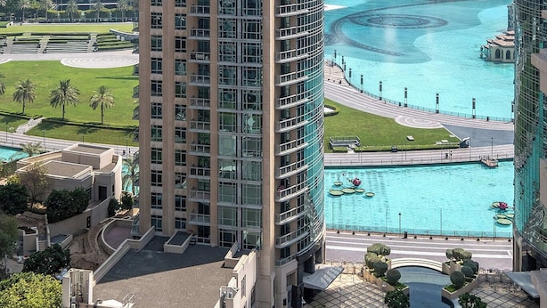 Un immeuble de grande hauteur au design moderne, entouré d’autres bâtiments imposants et agrémenté, au premier plan, d’une grande fontaine ou d’un autre élément aquatique.