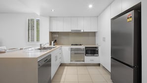 A modern kitchen with white cabinets, stainless steel appliances, and a large refrigerator. - Drift at Casuarina, Pool View - 14 (Tweed)