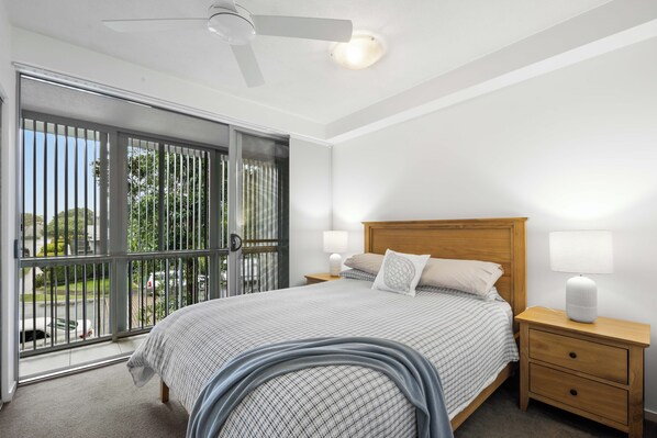 Un dormitorio con cama, mesitas de noche, ventilador de techo y vistas a través de una puerta corrediza de vidrio.