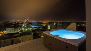 Un jacuzzi en un balcón con vista a la ciudad de noche.