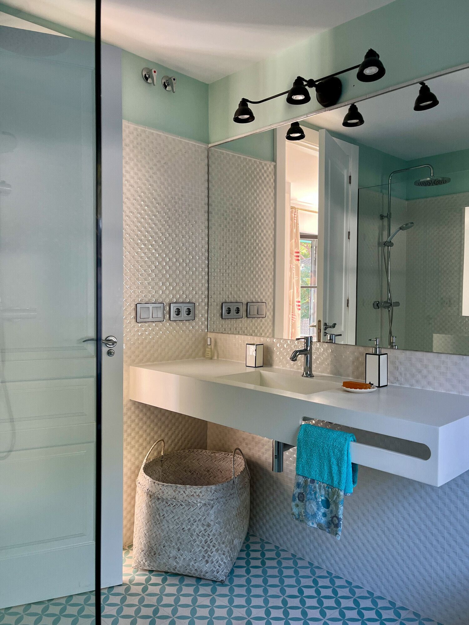 A bathroom with a large mirror, a shower, a sink, and a towel rack.