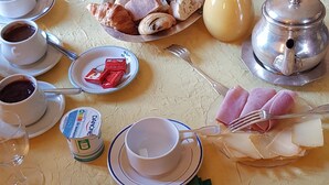 A breakfast setting with a variety of food items, including croissants, ham, and butter, along with coffee and tea. - Quiet, independent double room facing the forest (Saint-Nectaire)