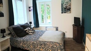 A bedroom with a bed, a nightstand, a dresser, a window with curtains, and a painting on the wall. - Quiet, independent double room facing the forest (Saint-Nectaire)