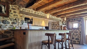 A rustic kitchen with a stone wall, wooden ceiling, and a bar area with stools.