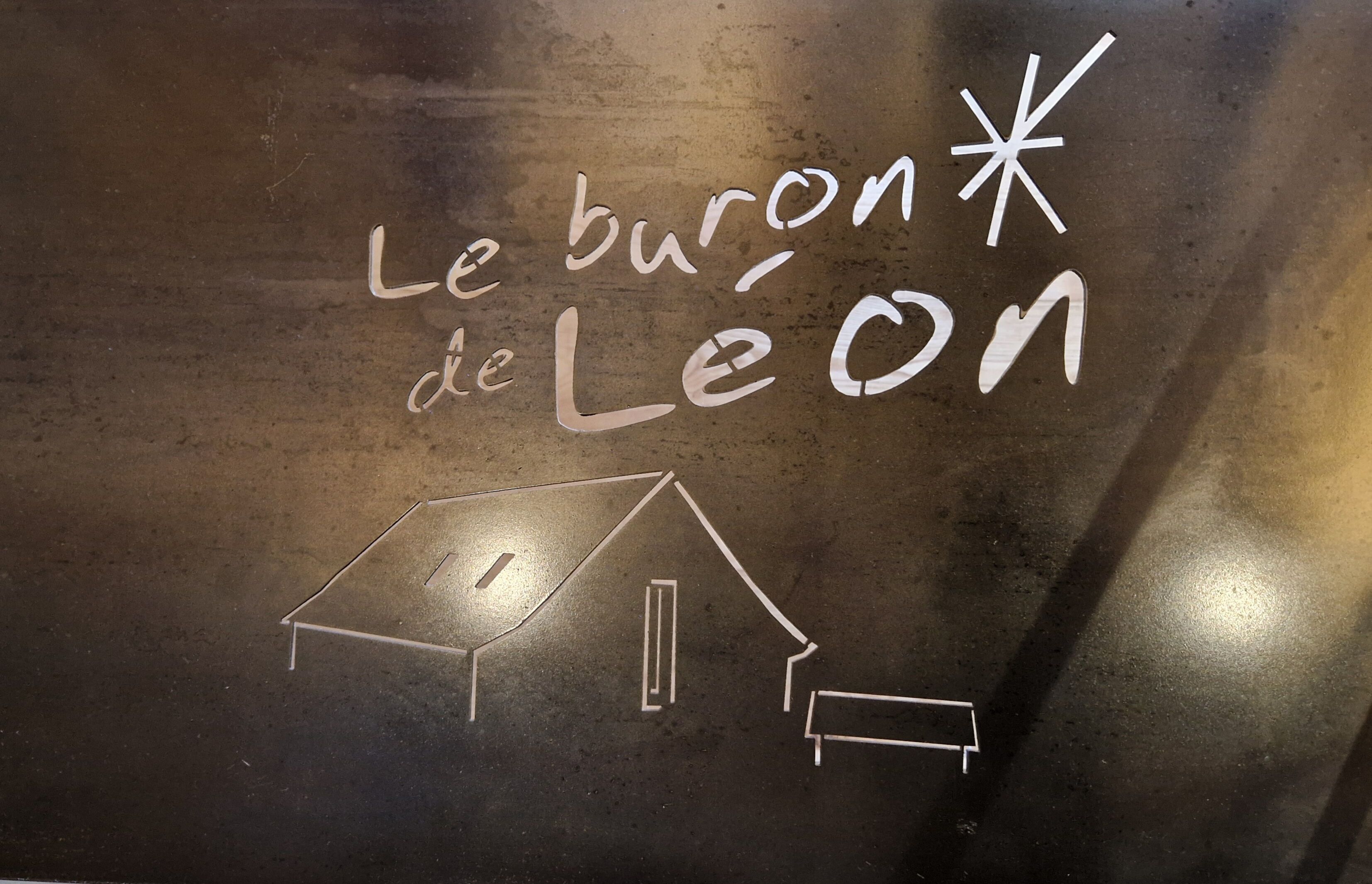A chalk drawing of a house with the text "Le buron de Leon" on a dark surface.
