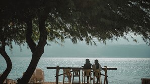 Une terrasse en bois avec des chaises donnant sur une étendue d’eau, un arbre offrant de l’ombre et une vue dégagée sur l’eau.