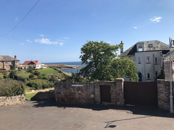 A coastal view with a stone wall, a gate, and buildings in the background. - Sandcastle Cottage, Crail with large garden on Fife Coastal Path by Roome Bay (Crail)