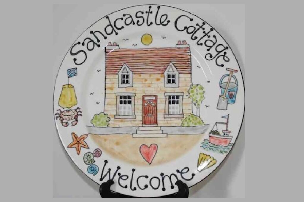 A plate with a drawing of a cottage labeled "Sandcastle Cottage" and "Welcome".