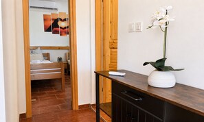 A hotel room with a bed, a bedside table with a remote control, a potted orchid, and a wall-mounted air conditioning unit.