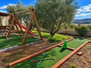 A miniature golf course with a wooden swing set and a red slide in the background. - Family Home Iskra (Bulic)