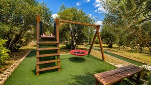 A playground with a wooden swing set, a climbing structure, and a red tire swing. - Family Home Iskra (Bulic)